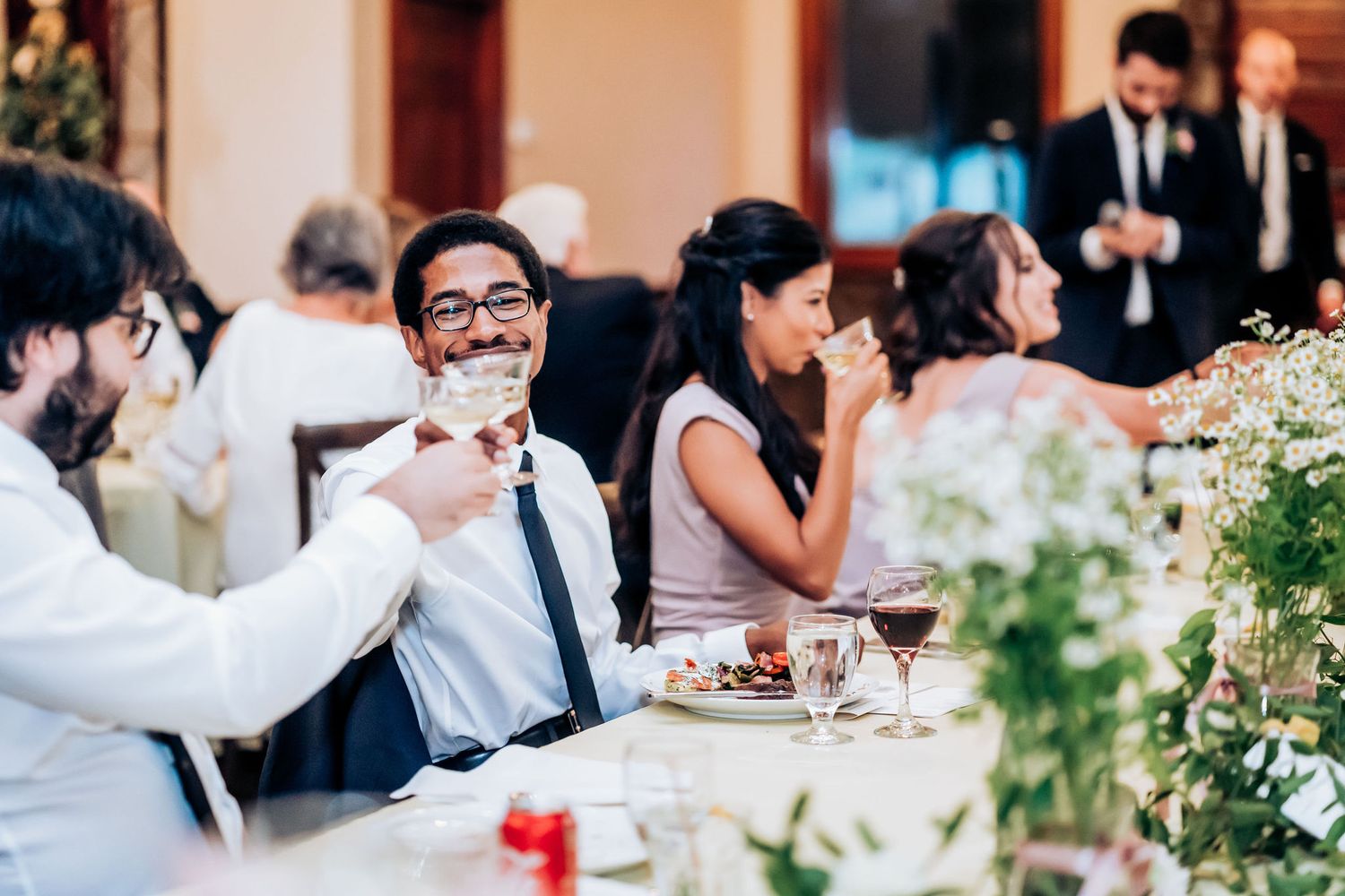 Wedding guests enjoying dinner at elegantly decorated reception tables with floral centerpieces.
