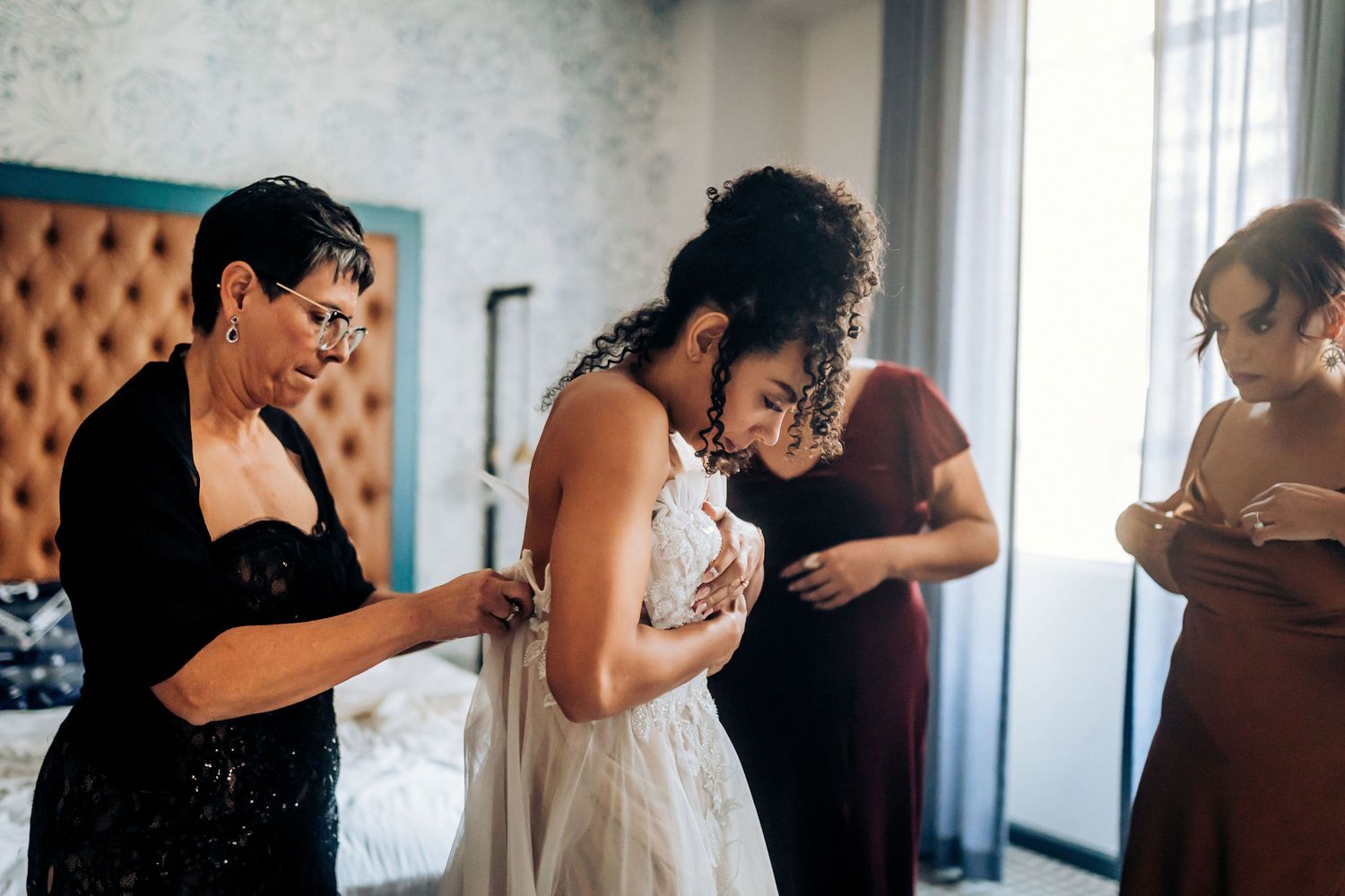 Getting ready scene with helpers assisting with wedding dress preparations.