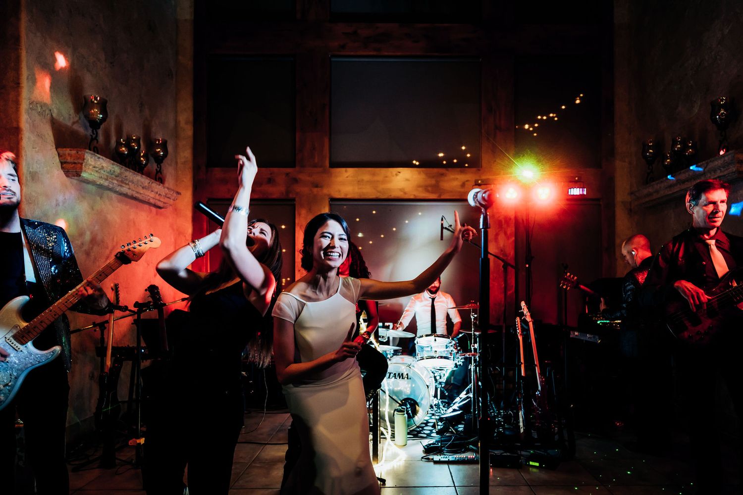 Live band performing on stage with dramatic red lighting and musicians playing instruments.