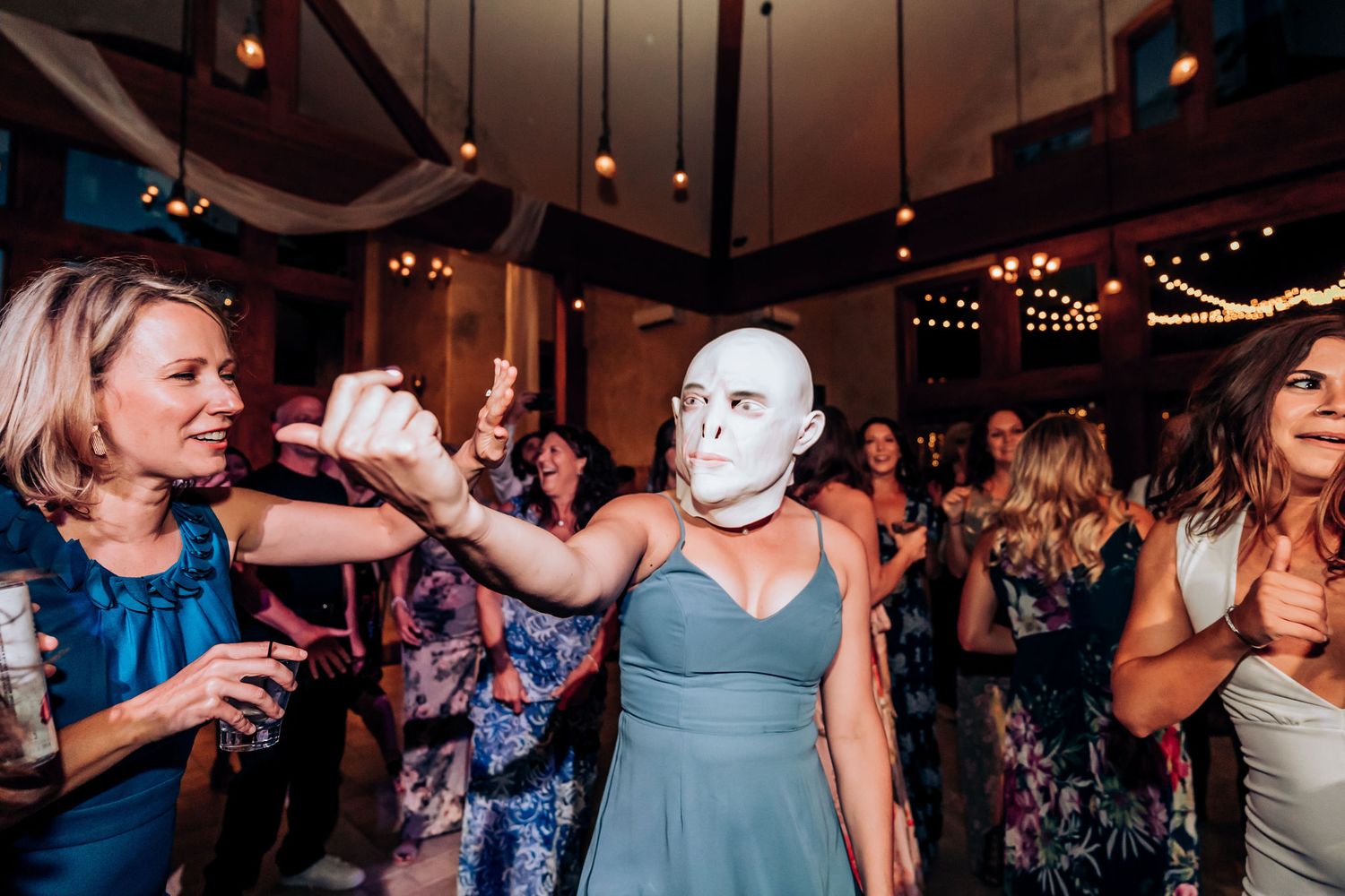 Guests dancing at a wedding reception in an indoor venue with string lights.
