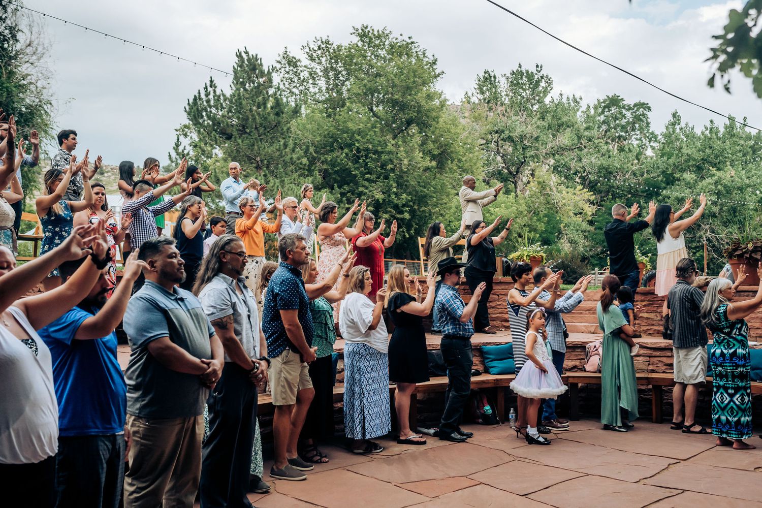 Large gathering of wedding guests with raised hands standing on outdoor deck during celebration.