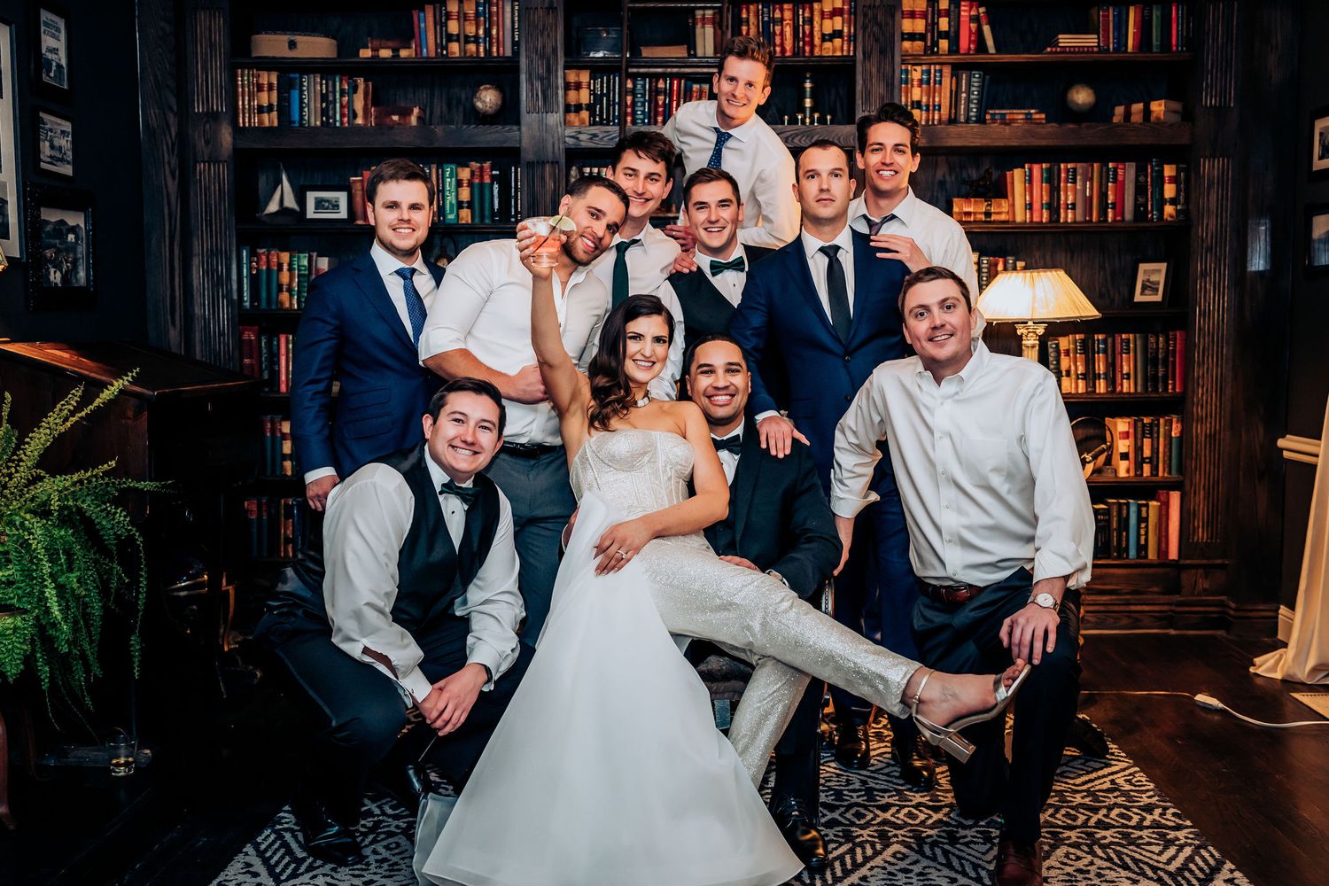 Wedding party poses together in front of library bookshelf backdrop for group photo.