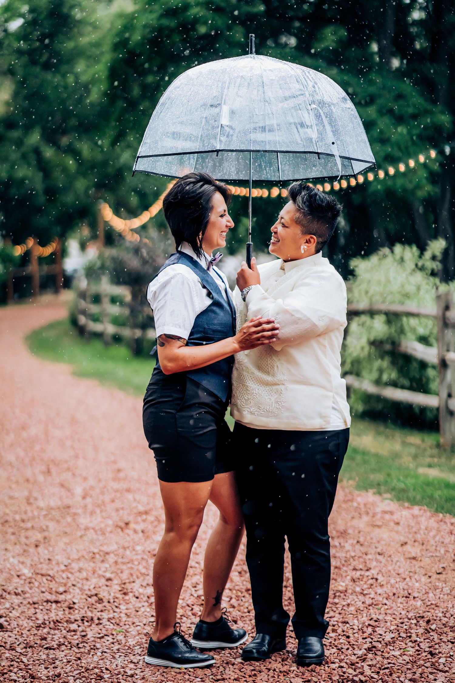 Couple sharing a tender moment under a clear umbrella on a gravel path.
