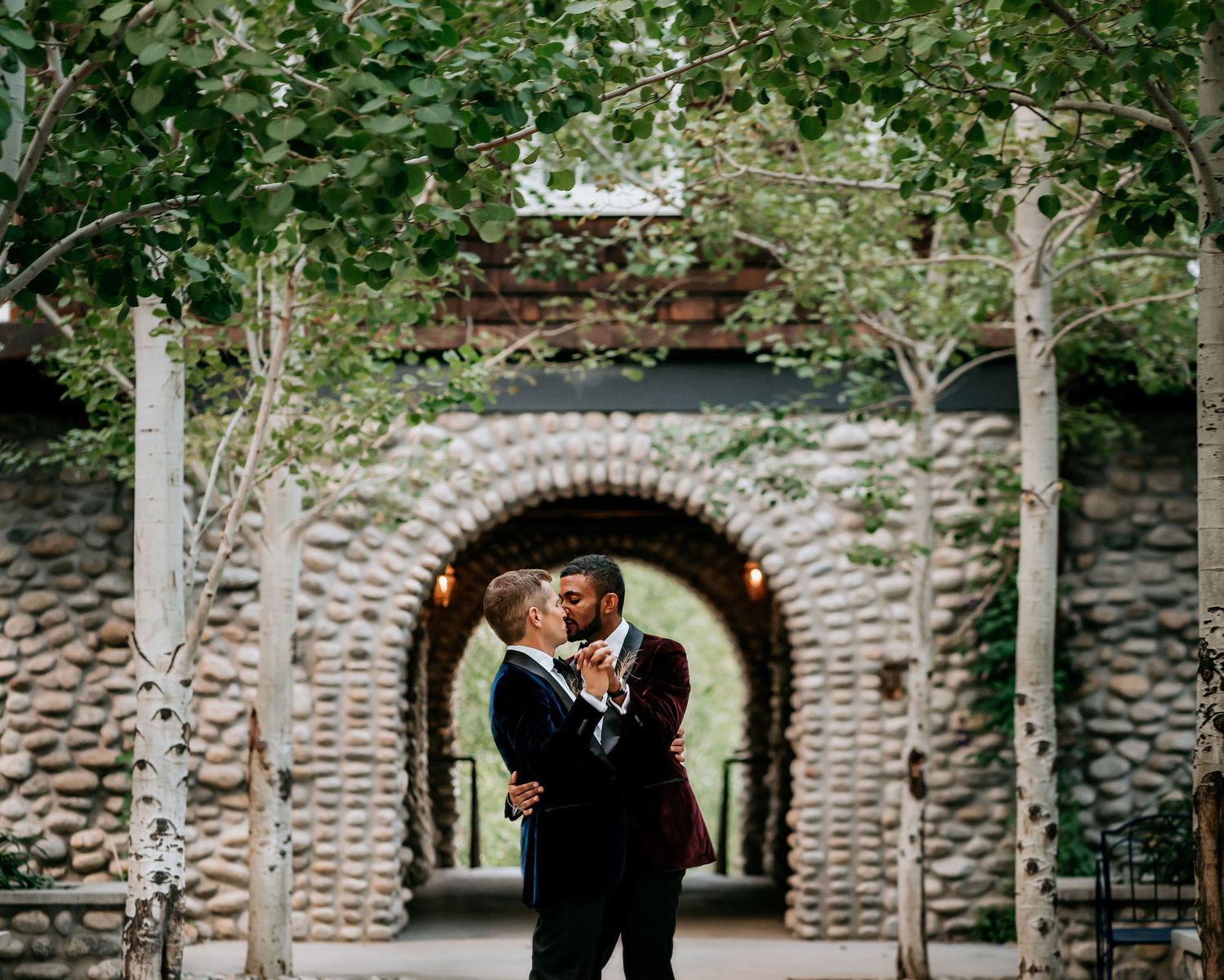 Elegant outdoor wedding ceremony at a stone archway surrounded by lush greenery.
