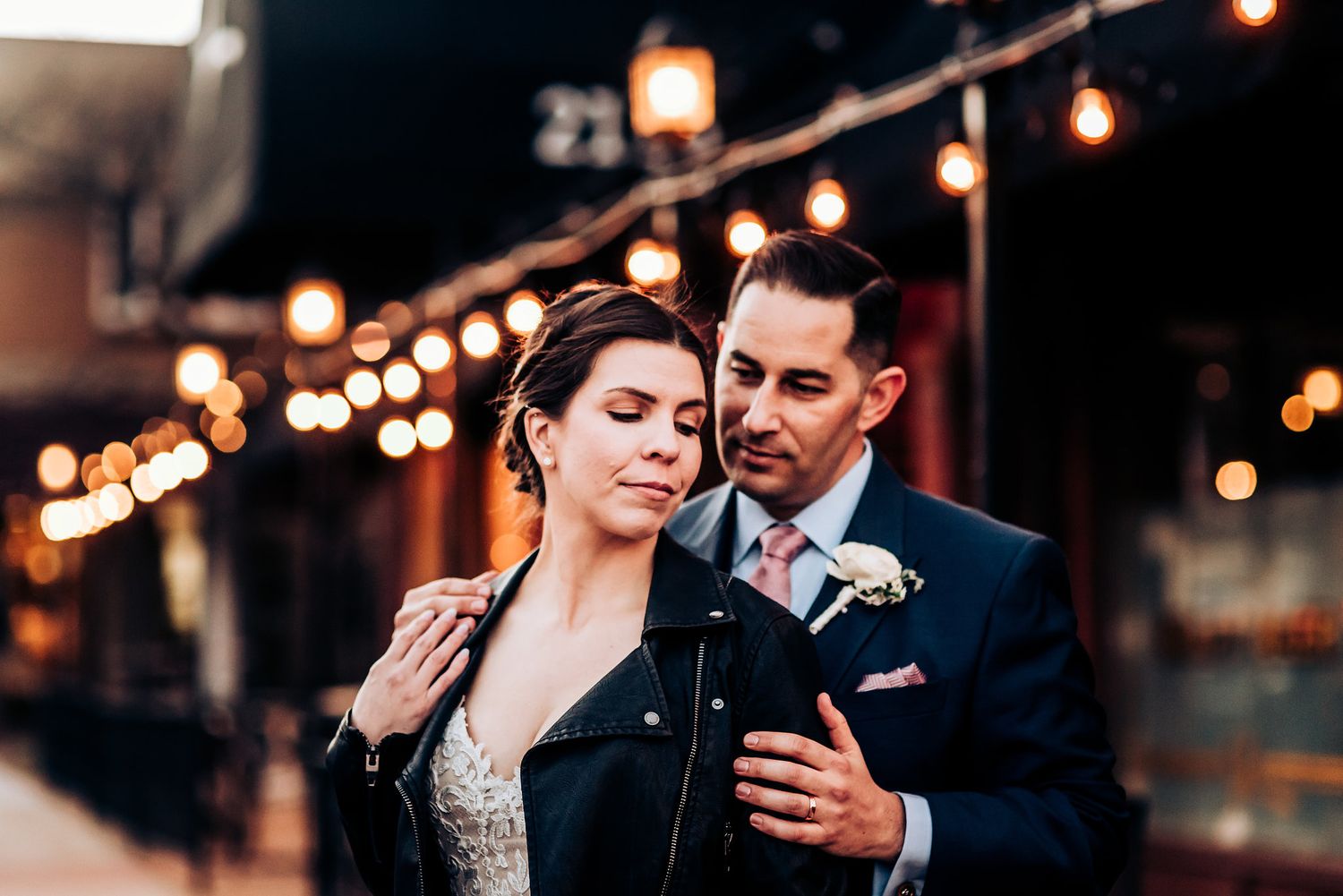 Romantic evening portrait with warm string lights and urban backdrop.