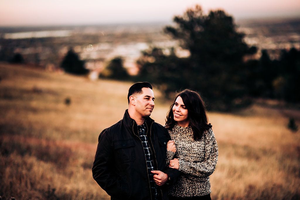 Romantic sunset portrait of a couple in casual wear against rolling hills and distant landscapes.