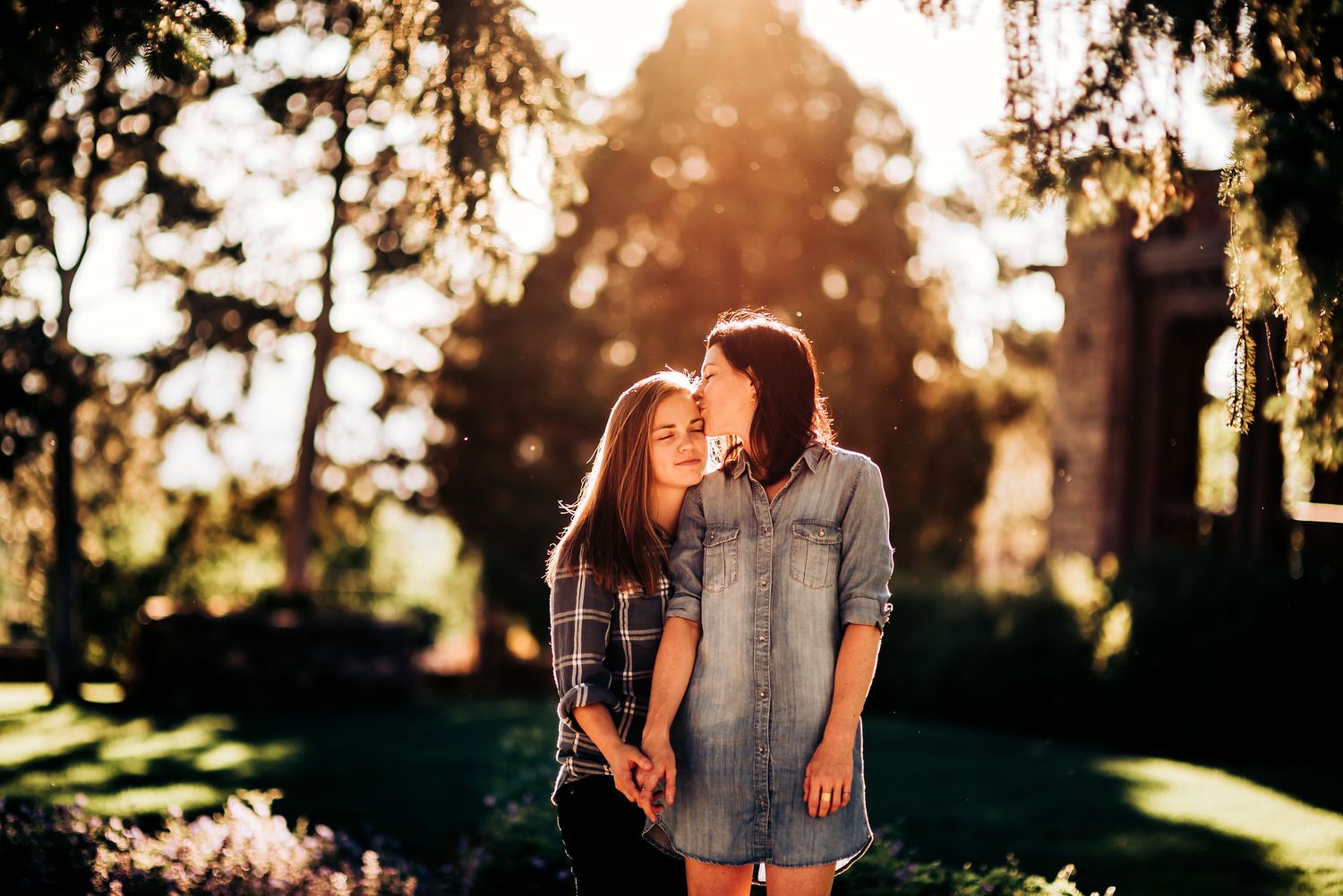 Two people stand together in golden evening light with trees and architecture in background.
