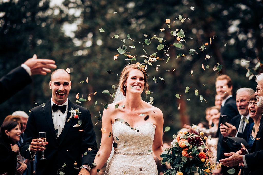 Wedding celebration with flower petals being tossed in the air during an outdoor forest ceremony.
