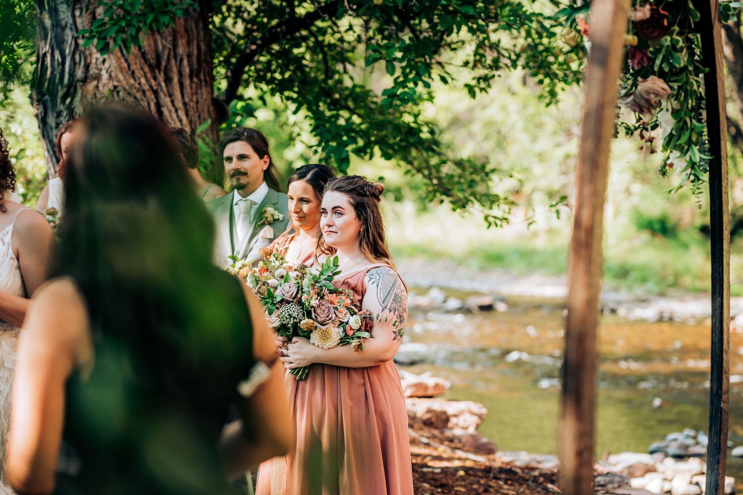 Wedding party members in formal attire holding bouquets outdoors.