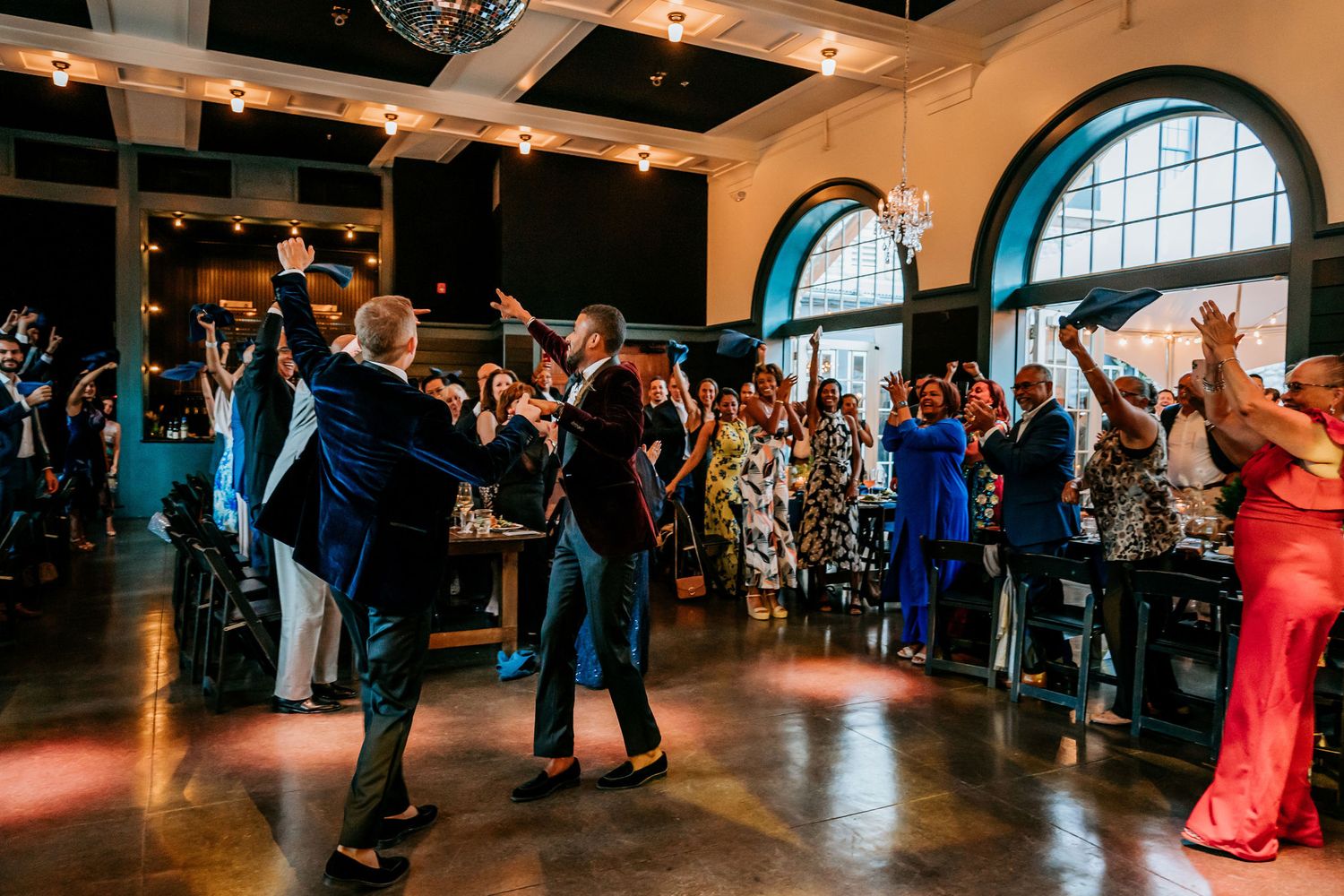 Wedding reception dance floor filled with guests celebrating under arched windows.