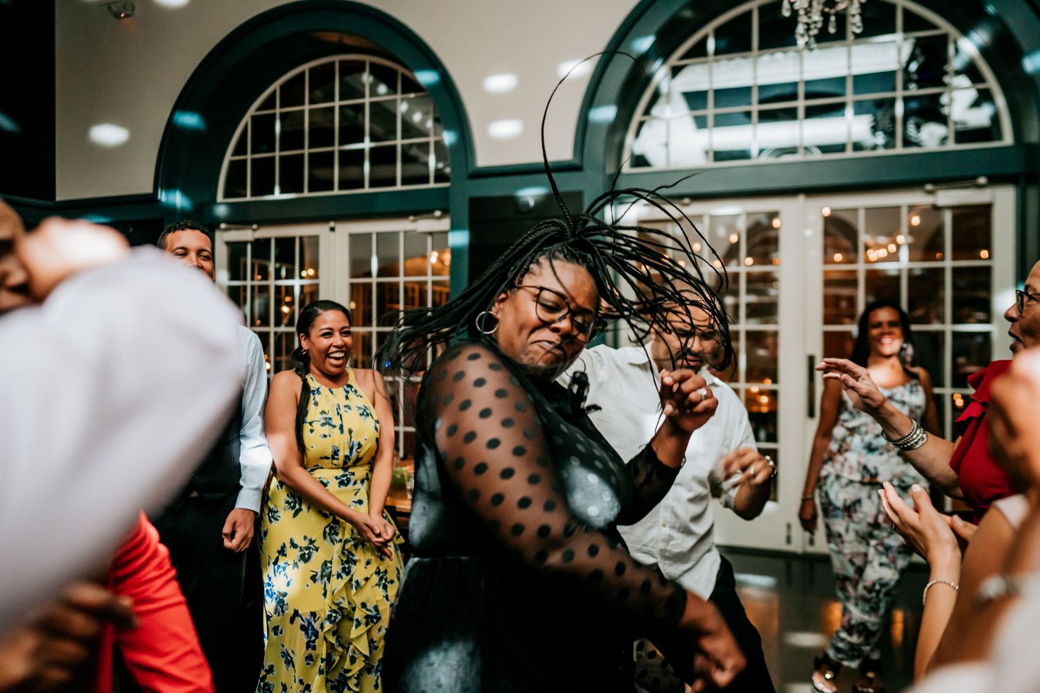 Wedding guests dance together under arched windows at an evening reception.