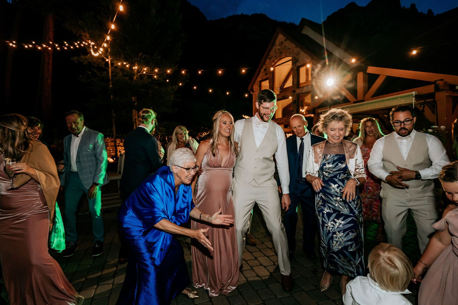 Wedding reception dance party under string lights with lively guests dancing outdoors.