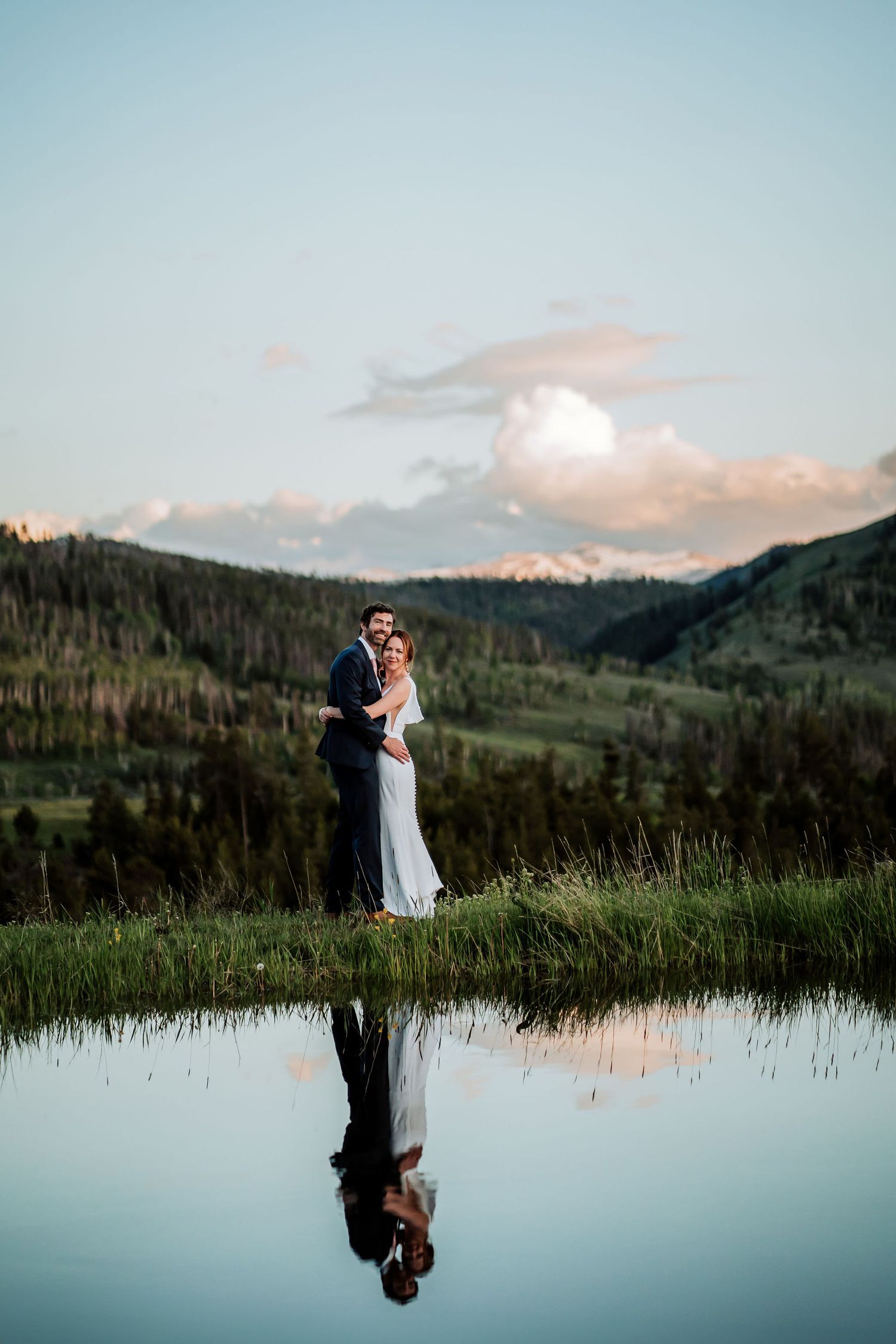 Sunset mountain wedding portrait with couple's reflection in peaceful lake.