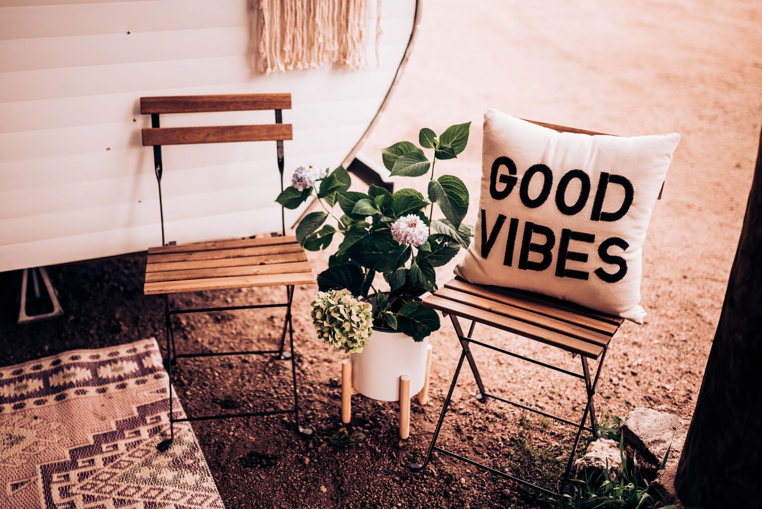 Minimalist outdoor seating area with Good Vibes pillow and potted plant against white wall.