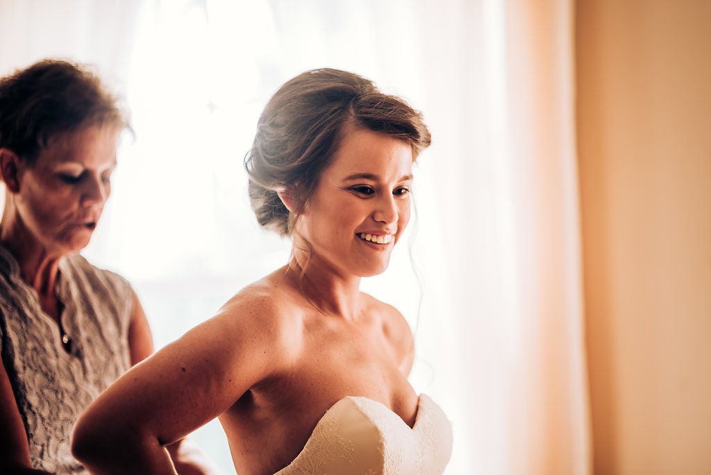 A close up shot of a woman in a white strapless dress smiling joyfully.