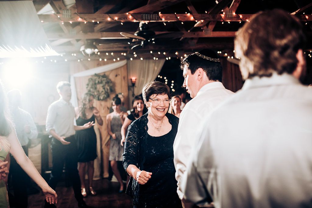 Partygoers dance under twinkling string lights at an indoor reception venue with festive atmosphere.