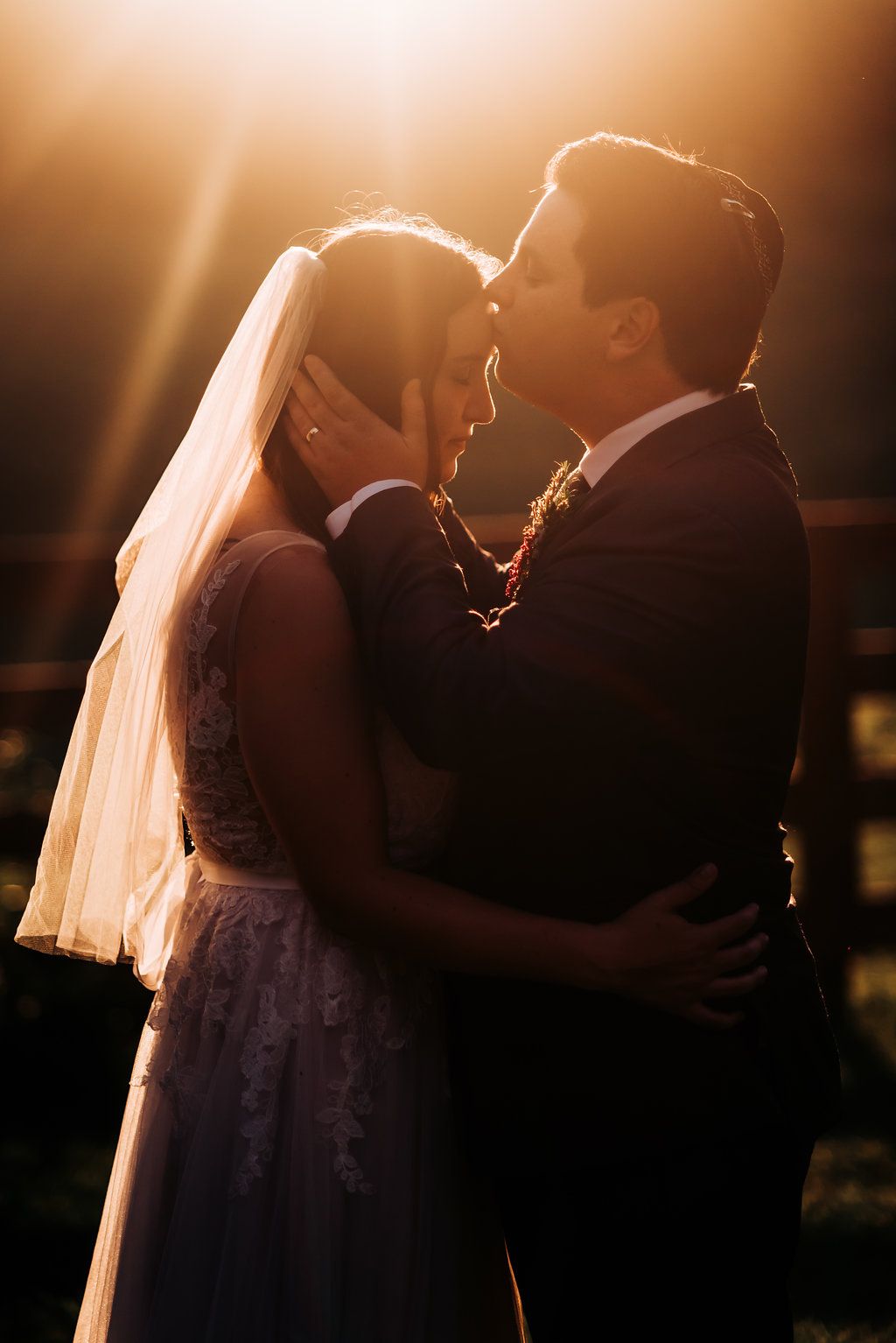 Backlit wedding couple embracing in warm sunset light.