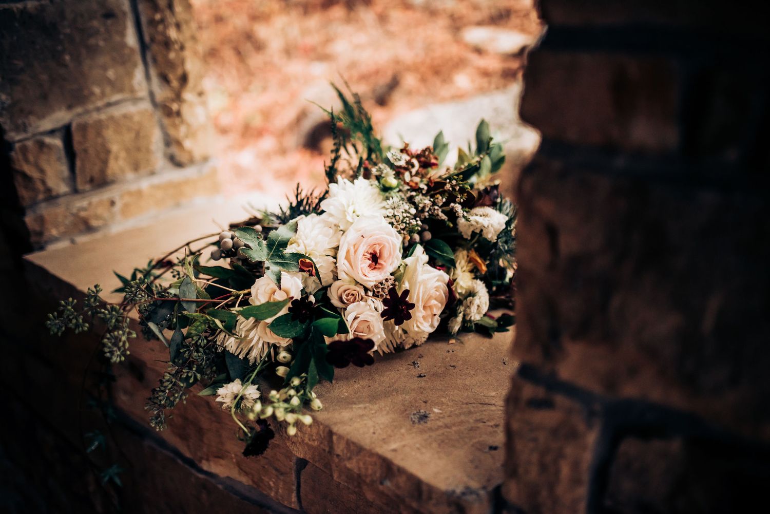 Romantic floral wedding bouquet with pale pink roses and greenery resting on rustic stone ledge.