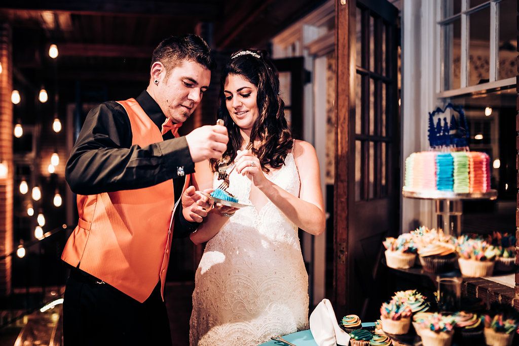 Couple sharing cake at their wedding reception by a dessert display with festive lighting.