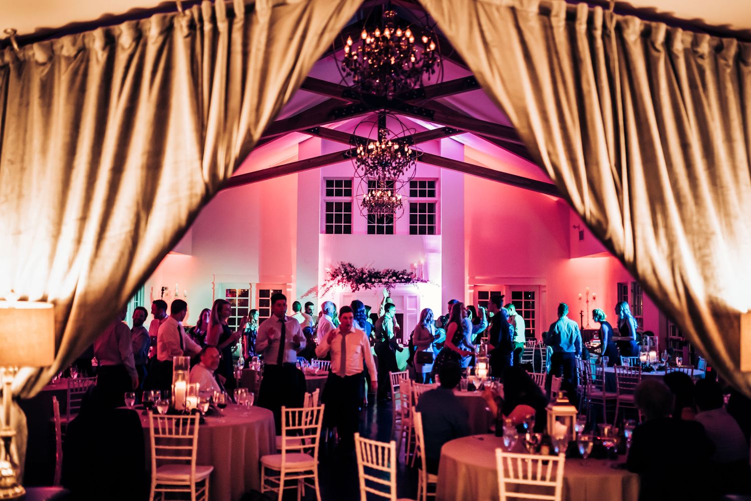 Pink-lit wedding reception venue with draped fabric and elegant chiavari chairs.