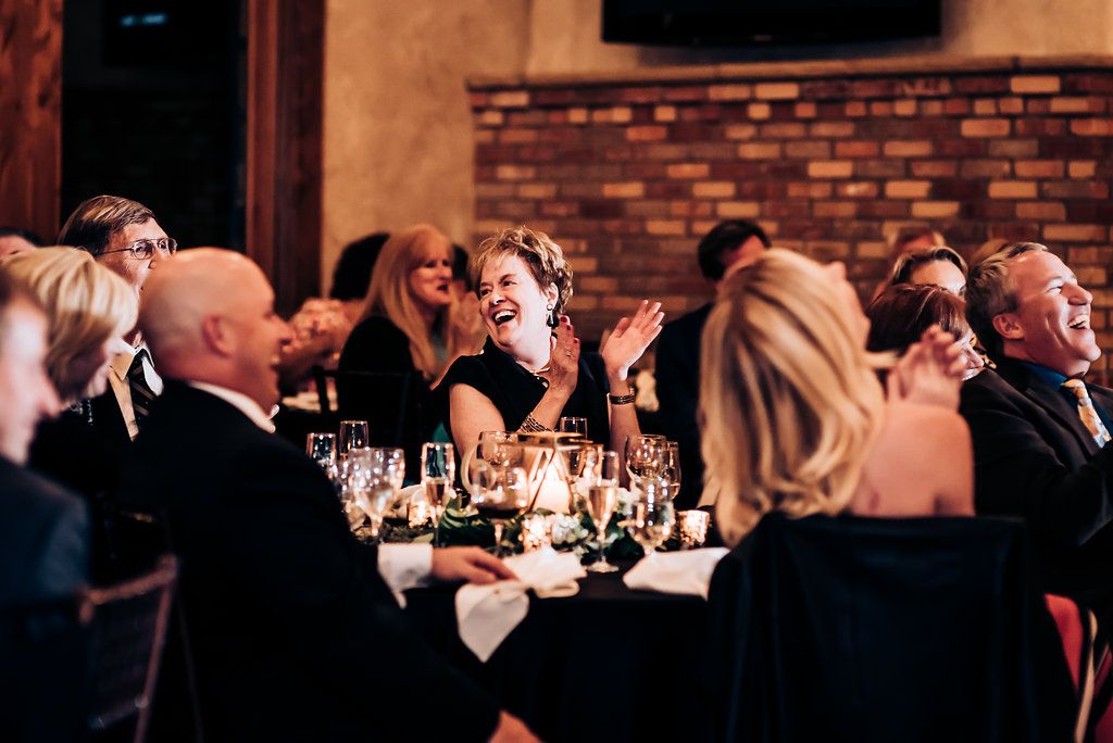 Wedding guests laugh and socialize at elegant reception dinner tables.