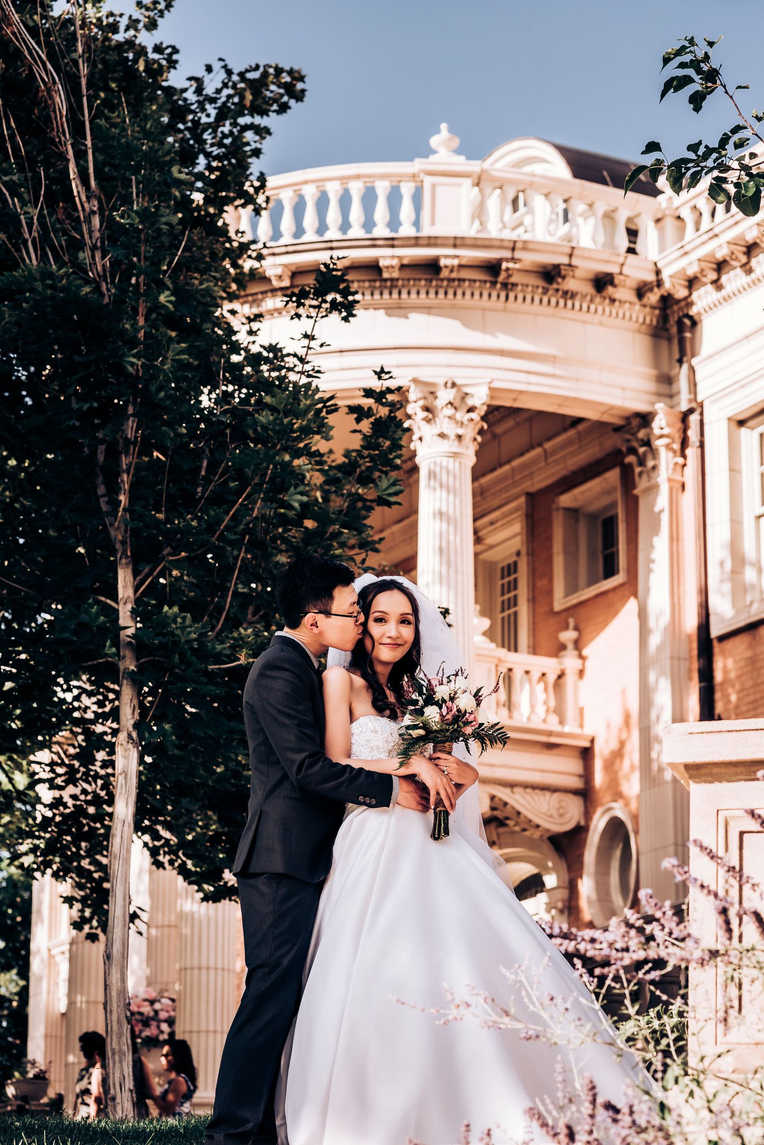 A romantic wedding portrait against elegant architecture with white balustrade and columns.