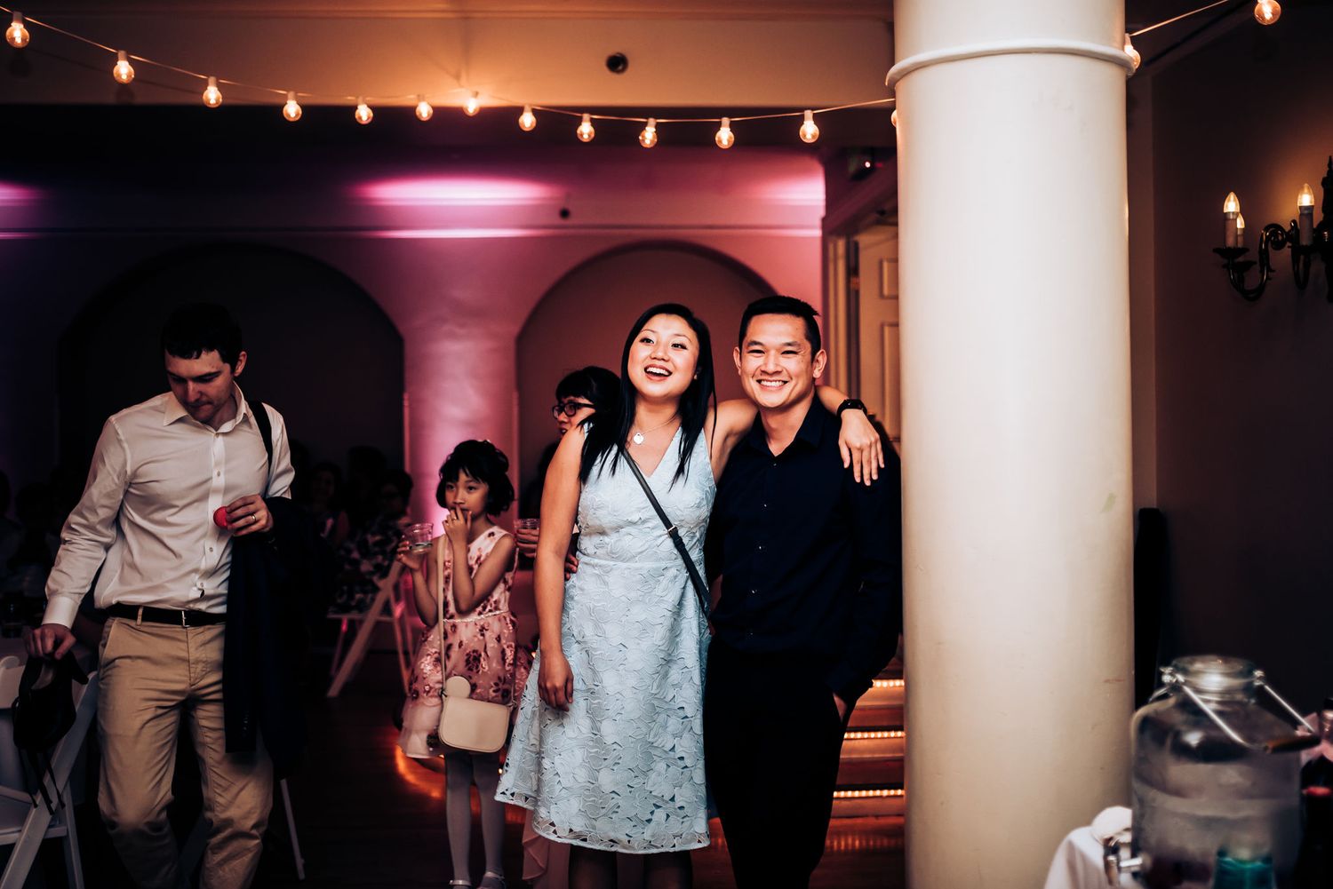 Wedding guests dancing and celebrating under string lights at an indoor reception.