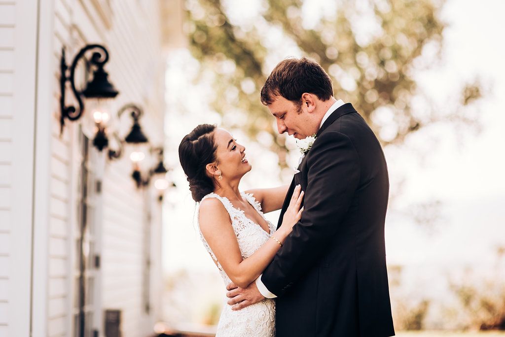 Romantic wedding couple embrace in front of white building with vintage lanterns.