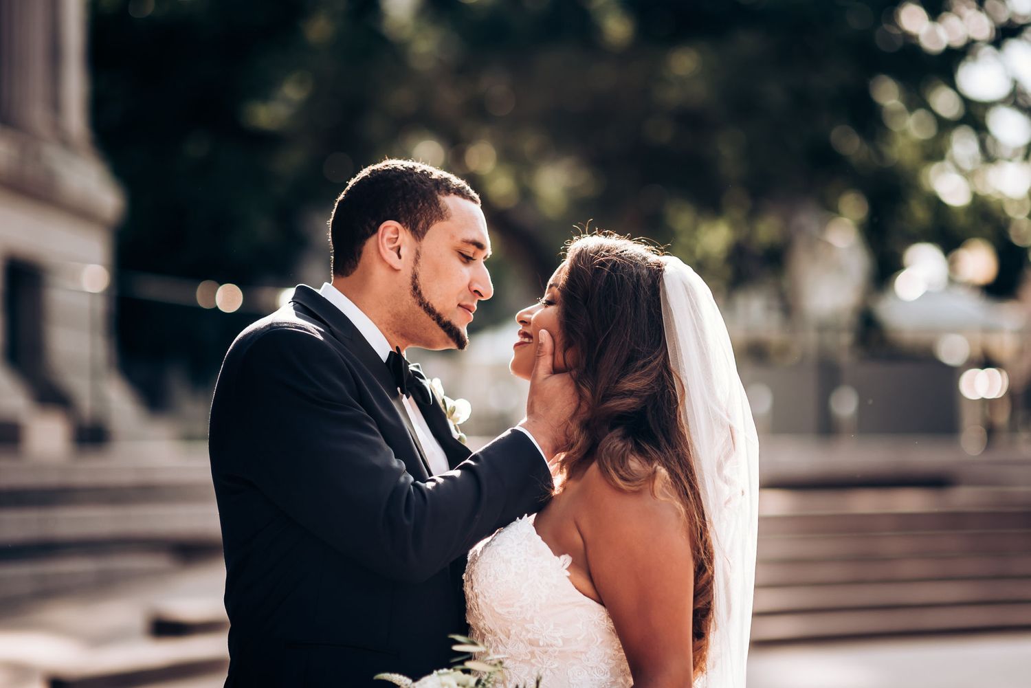 Tender moment between newlyweds against architectural backdrop.