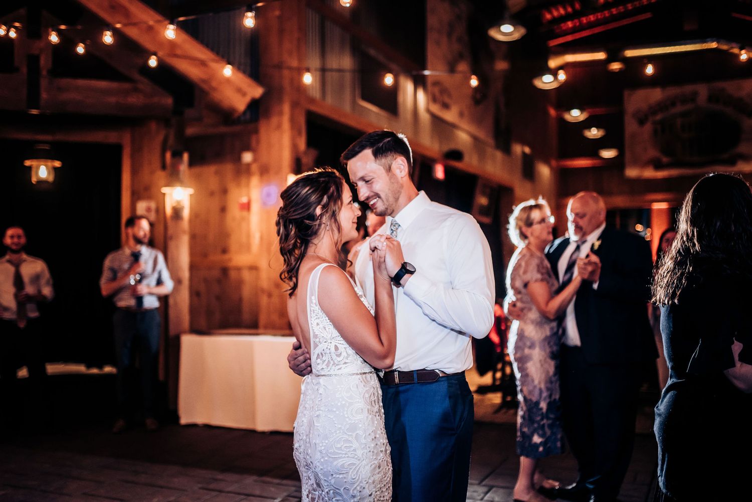 Couple shares their first dance in a warmly lit rustic reception venue.