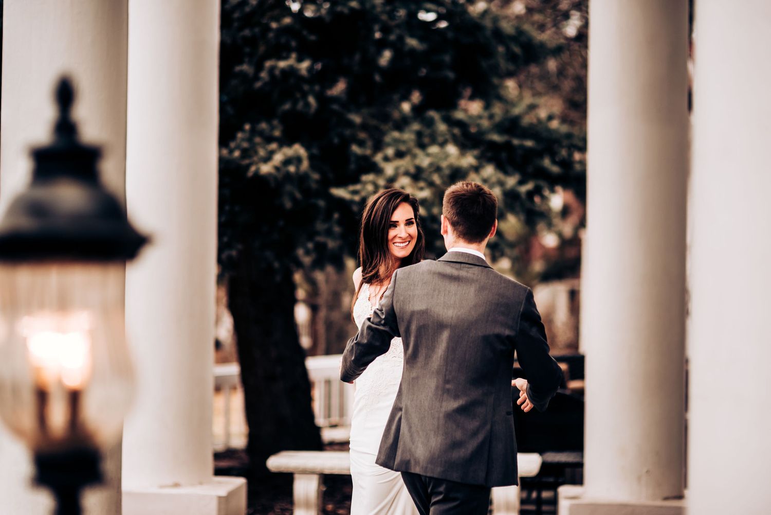 Elegant wedding couple shares a tender moment between classic white columns with lantern lighting.