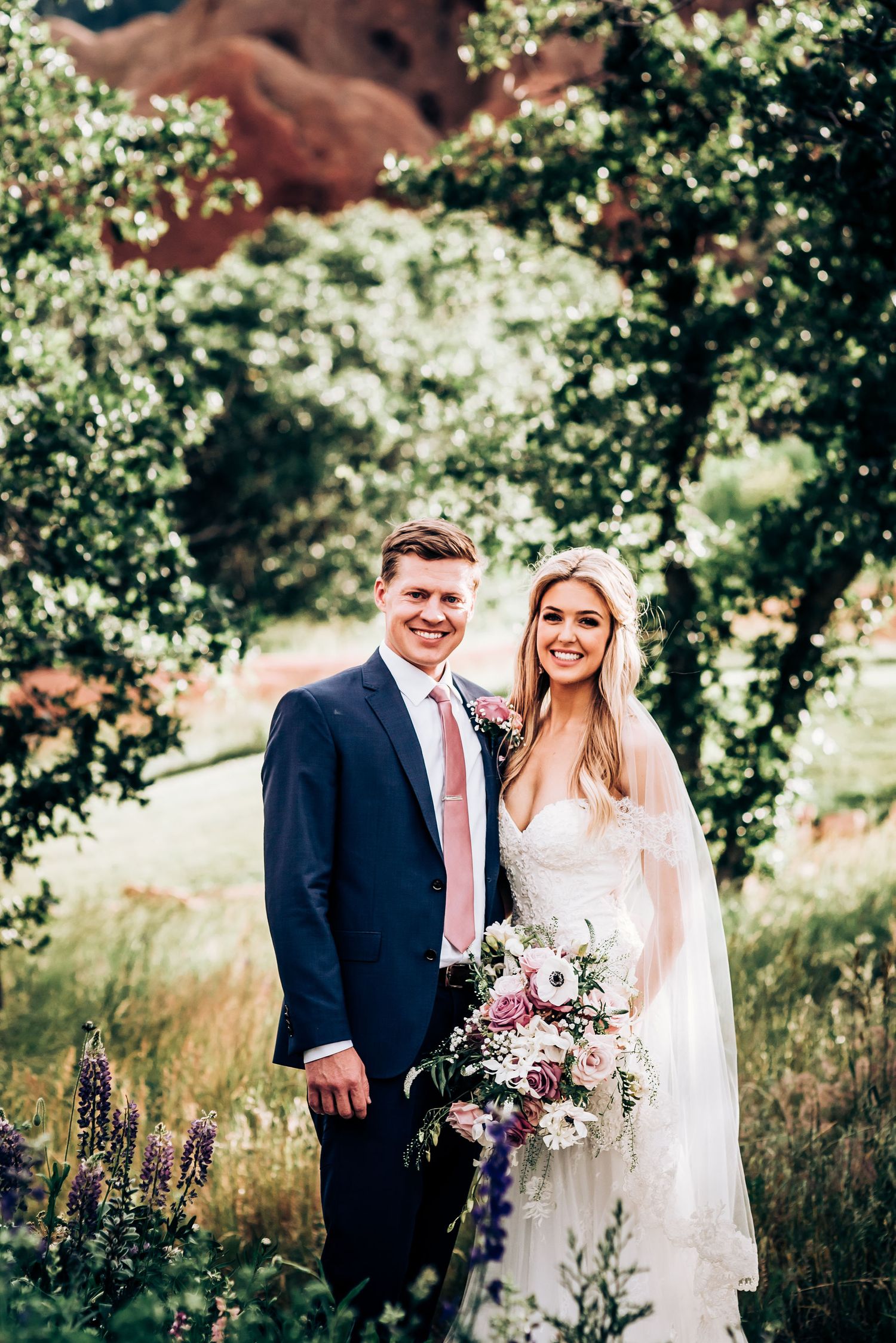Couple poses in garden setting with red rock formations in background.