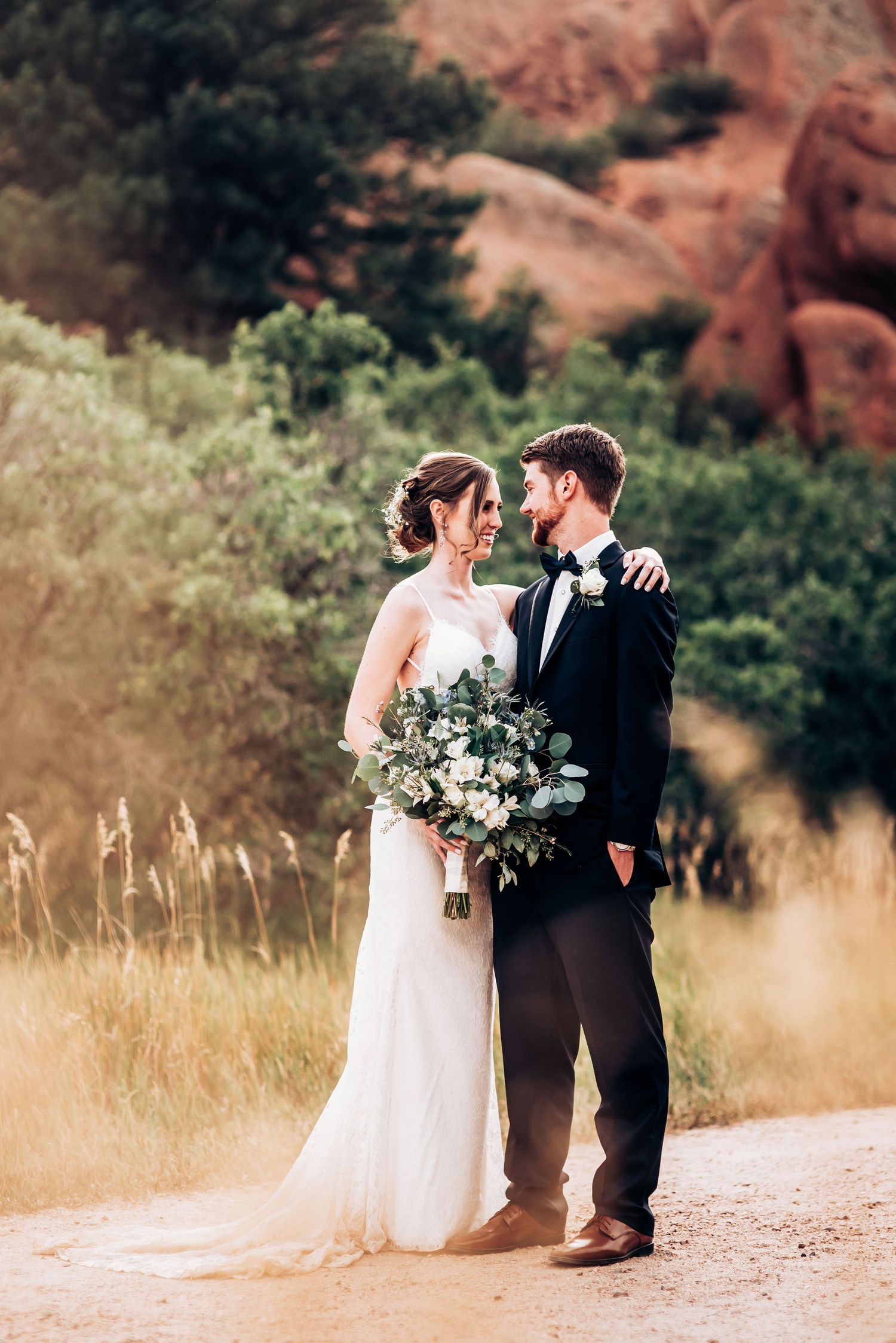Wedding portrait on dirt path with red rocks and golden grass in background.
