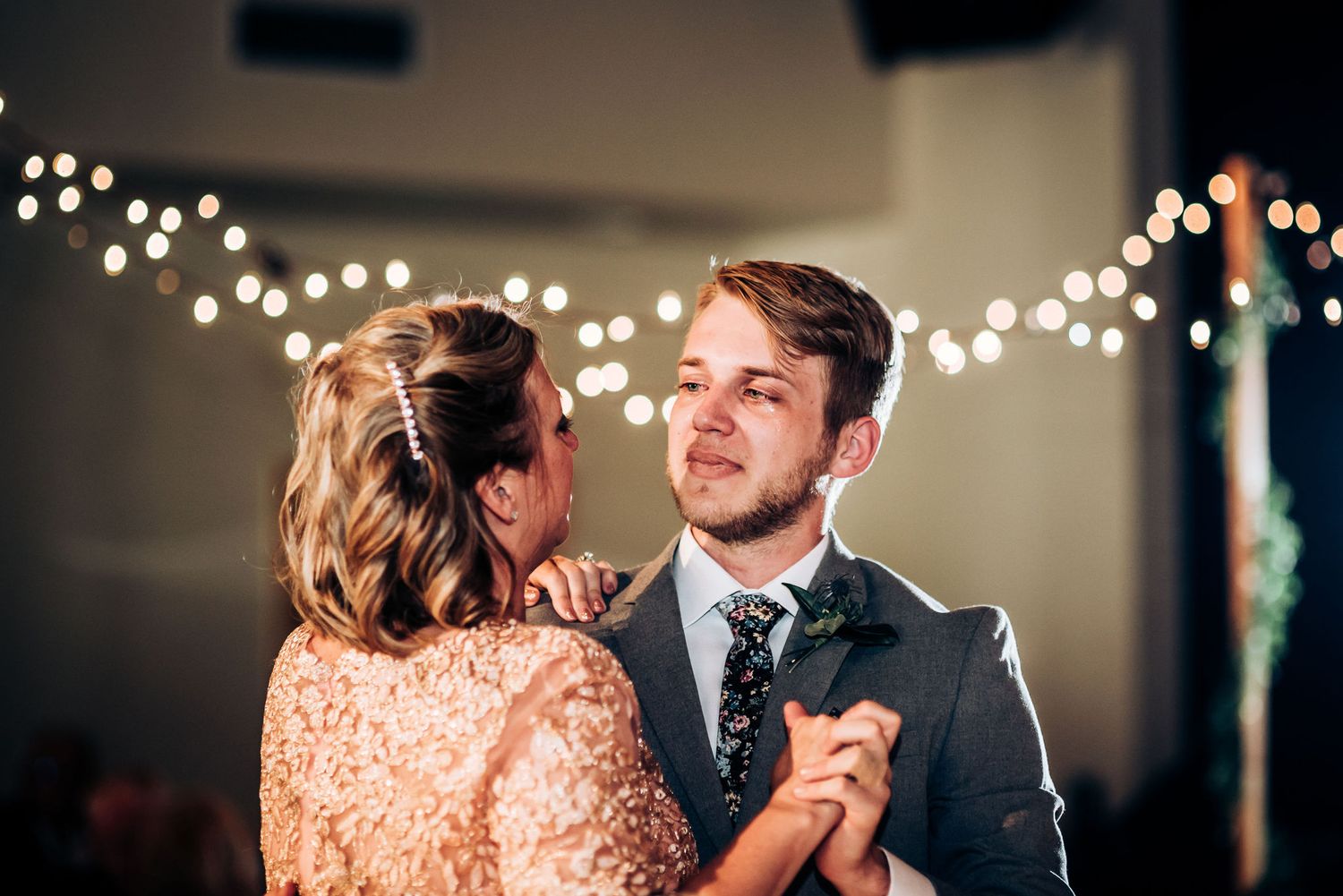 Romantic slow dance moment captured under decorative string lights at indoor reception.