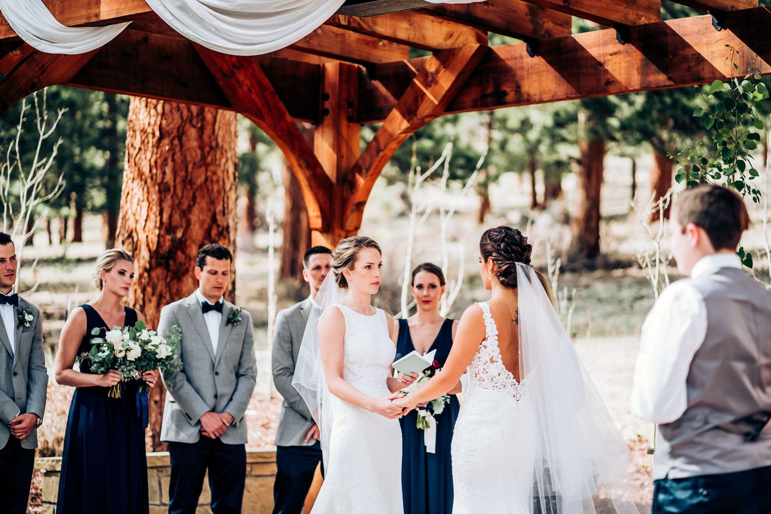 Intimate wedding ceremony moment under a rustic wooden arbor with white draping.
