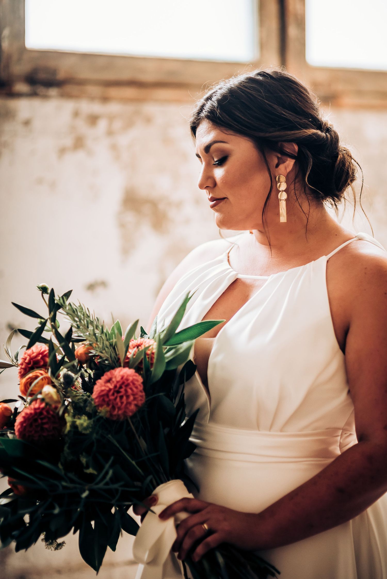 Side profile of bride in halter wedding dress with elegant updo and statement earrings.