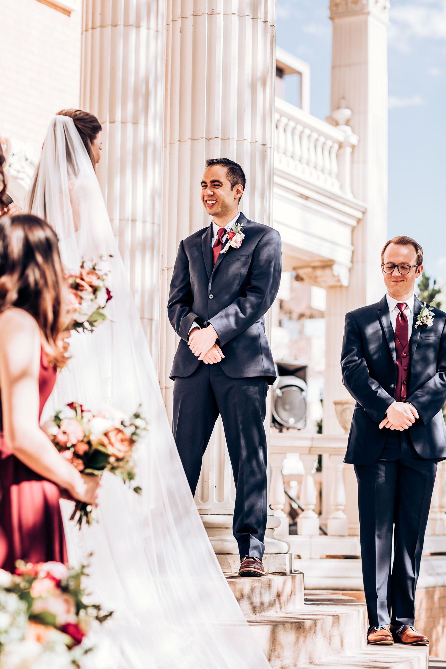 Elegant outdoor wedding ceremony on stone steps with classical columns in the background.