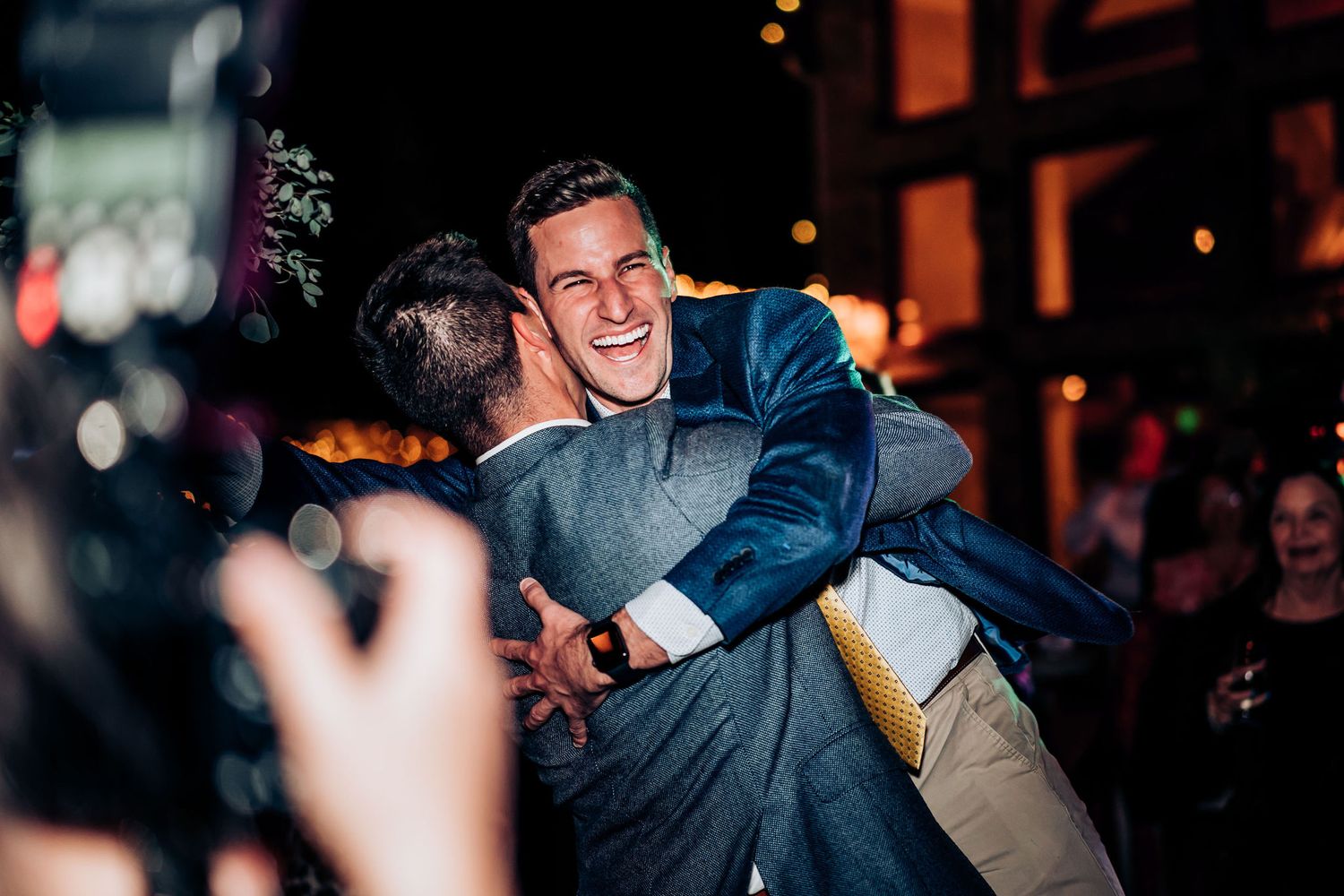 Two guests share an emotional embrace during nighttime wedding celebration.