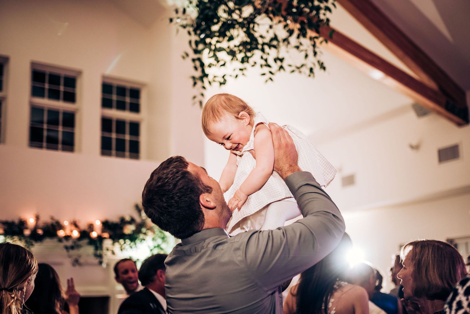 Touching moment at wedding reception as baby is lifted high in celebration.