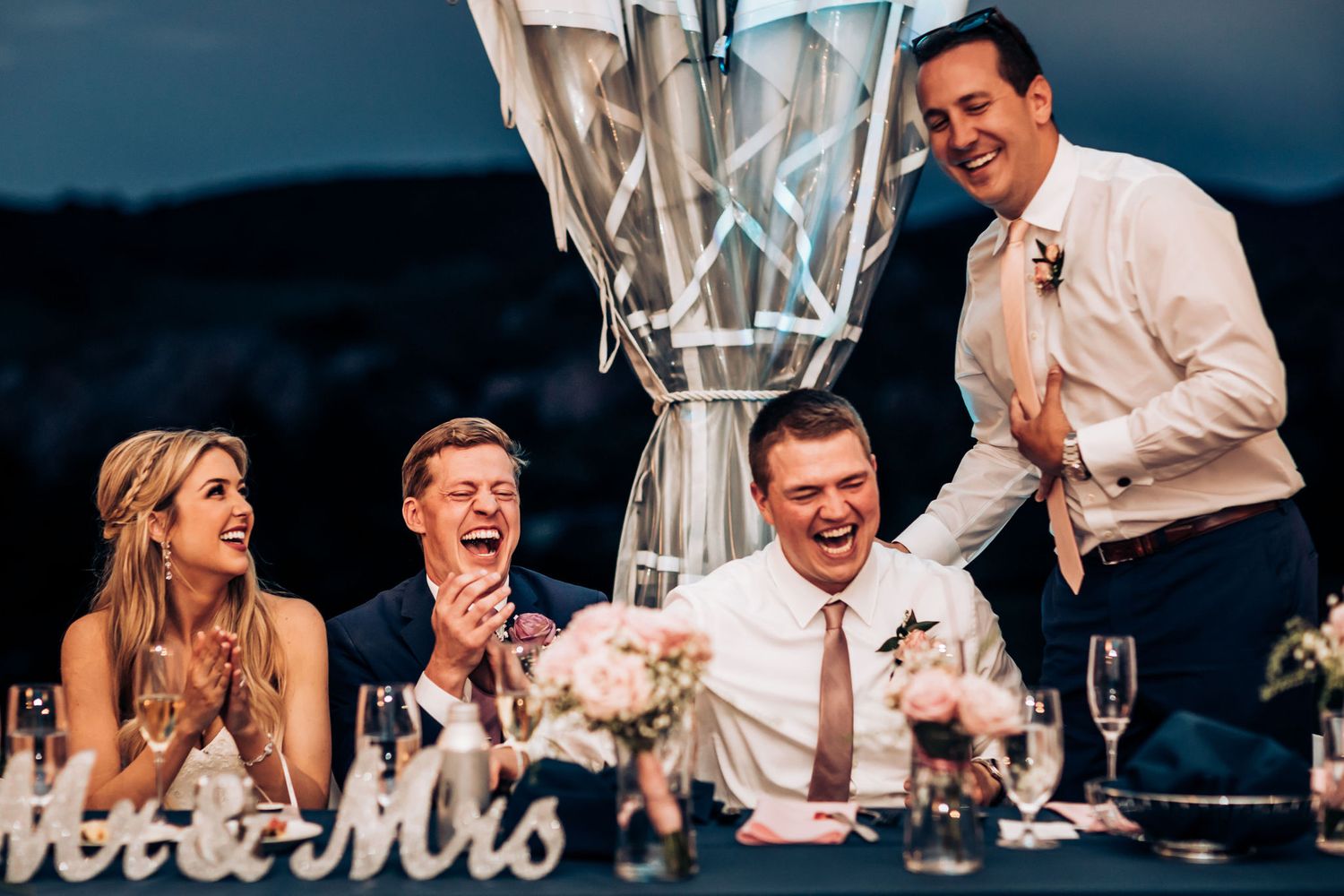 Candid laughter moment during wedding reception speeches at head table.