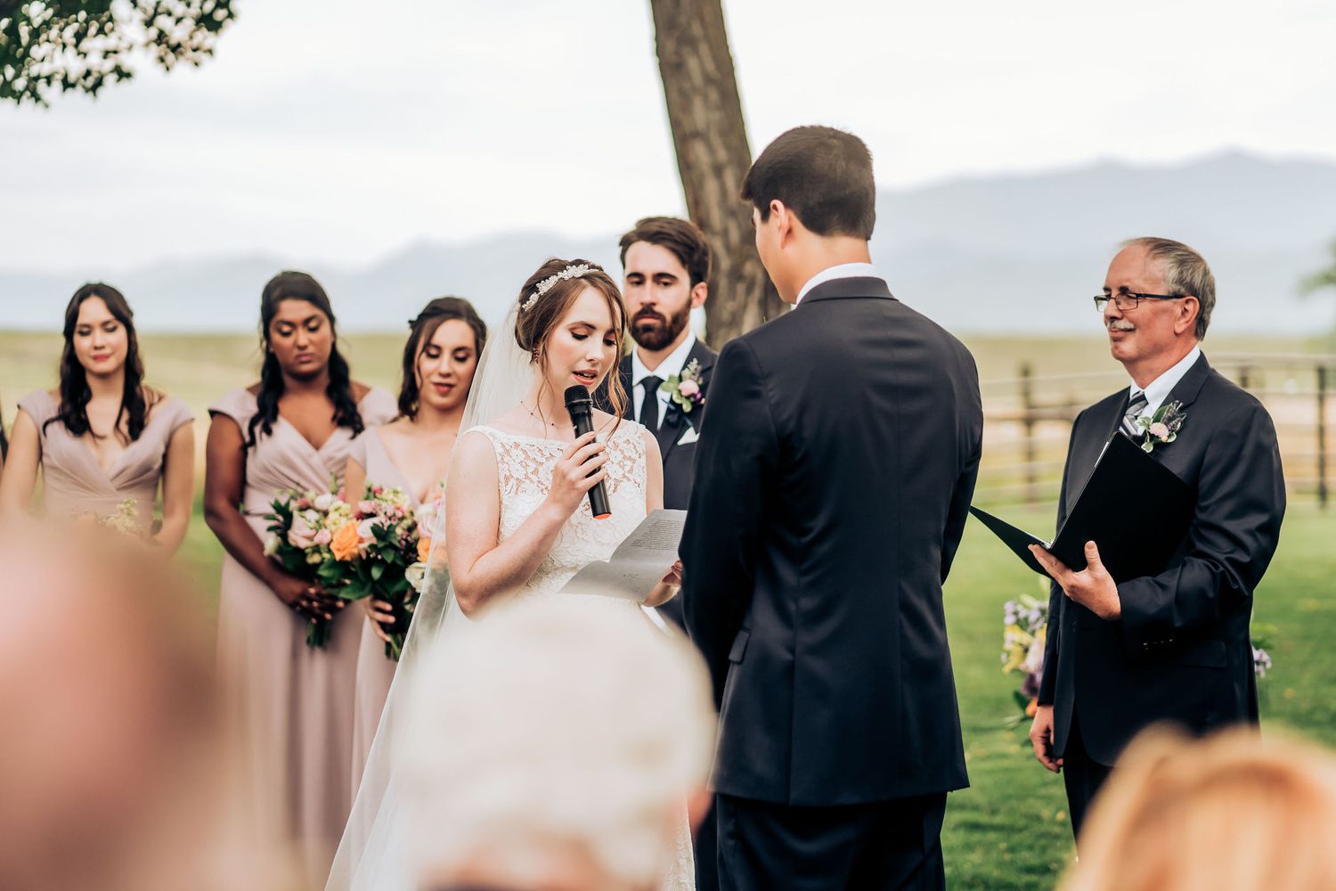 Couple exchanging vows during outdoor ceremony with wedding party and officiant looking on.