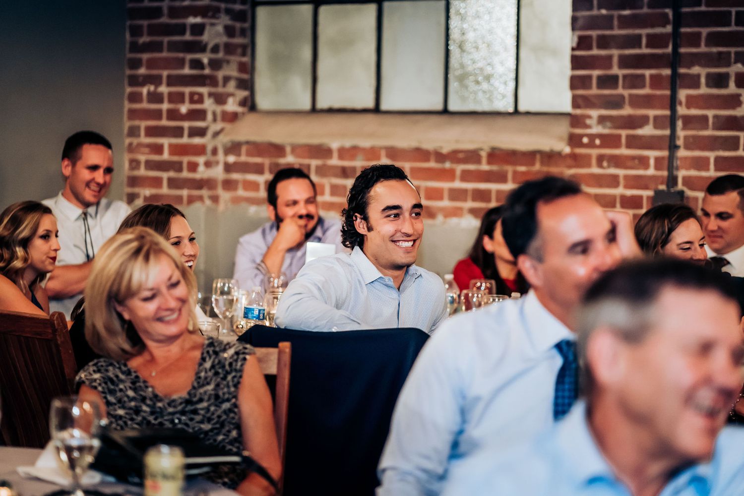 Candid shot of wedding guests laughing during reception speeches.