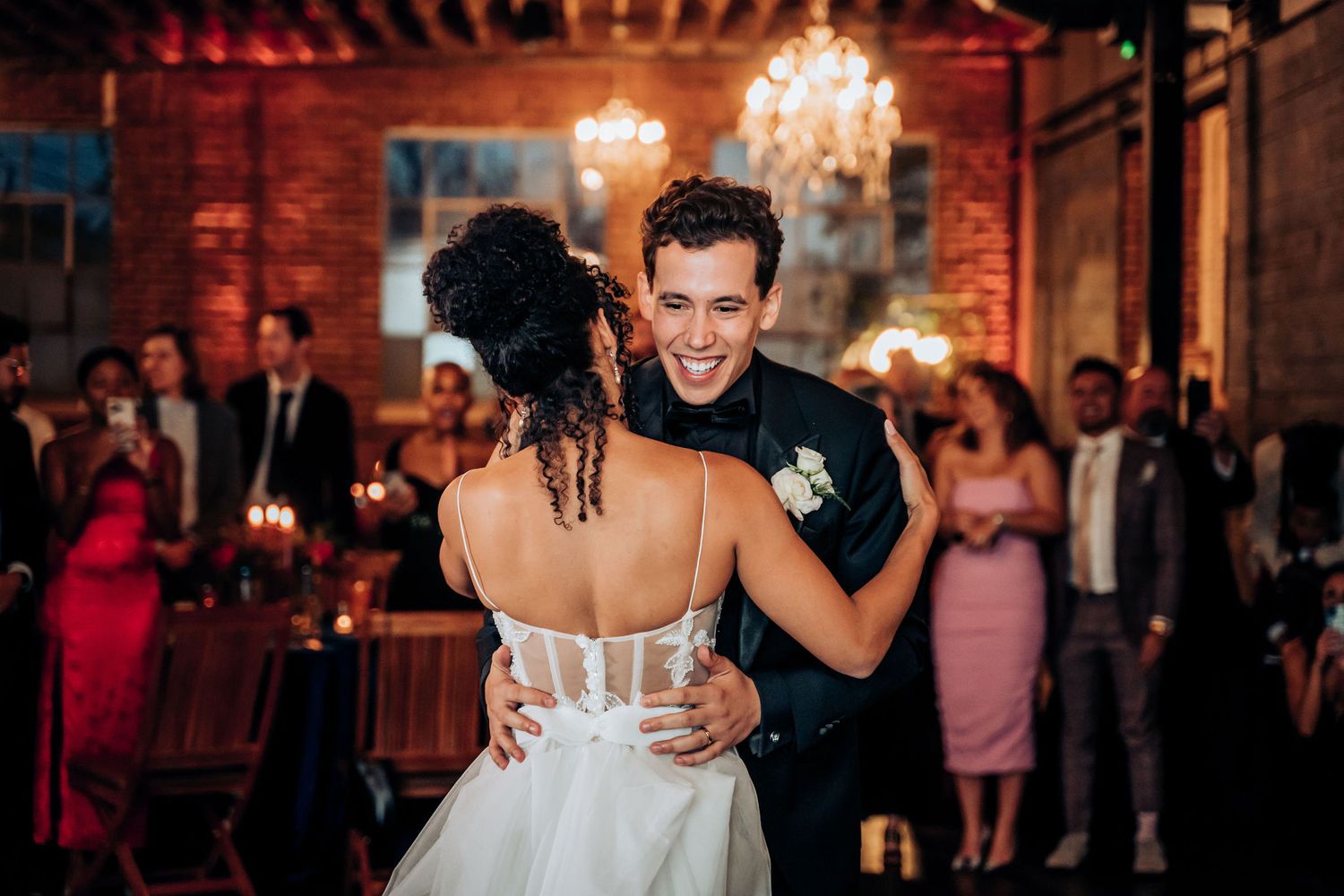 Couple sharing intimate dance at wedding reception in rustic venue with ambient lighting.