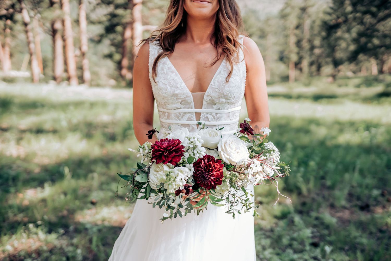 A beautiful wedding bouquet with burgundy and white flowers held against a white bridal gown.