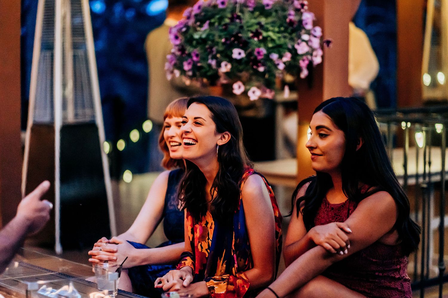 Party guests enjoying conversation at an outdoor evening reception with hanging floral decorations.
