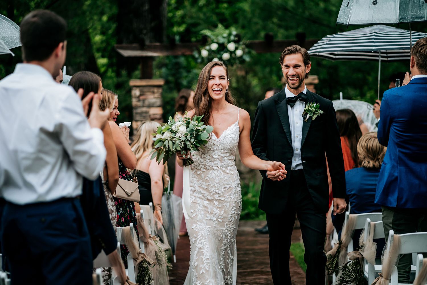 Newlyweds walk down the aisle while guests celebrate at outdoor wedding ceremony.