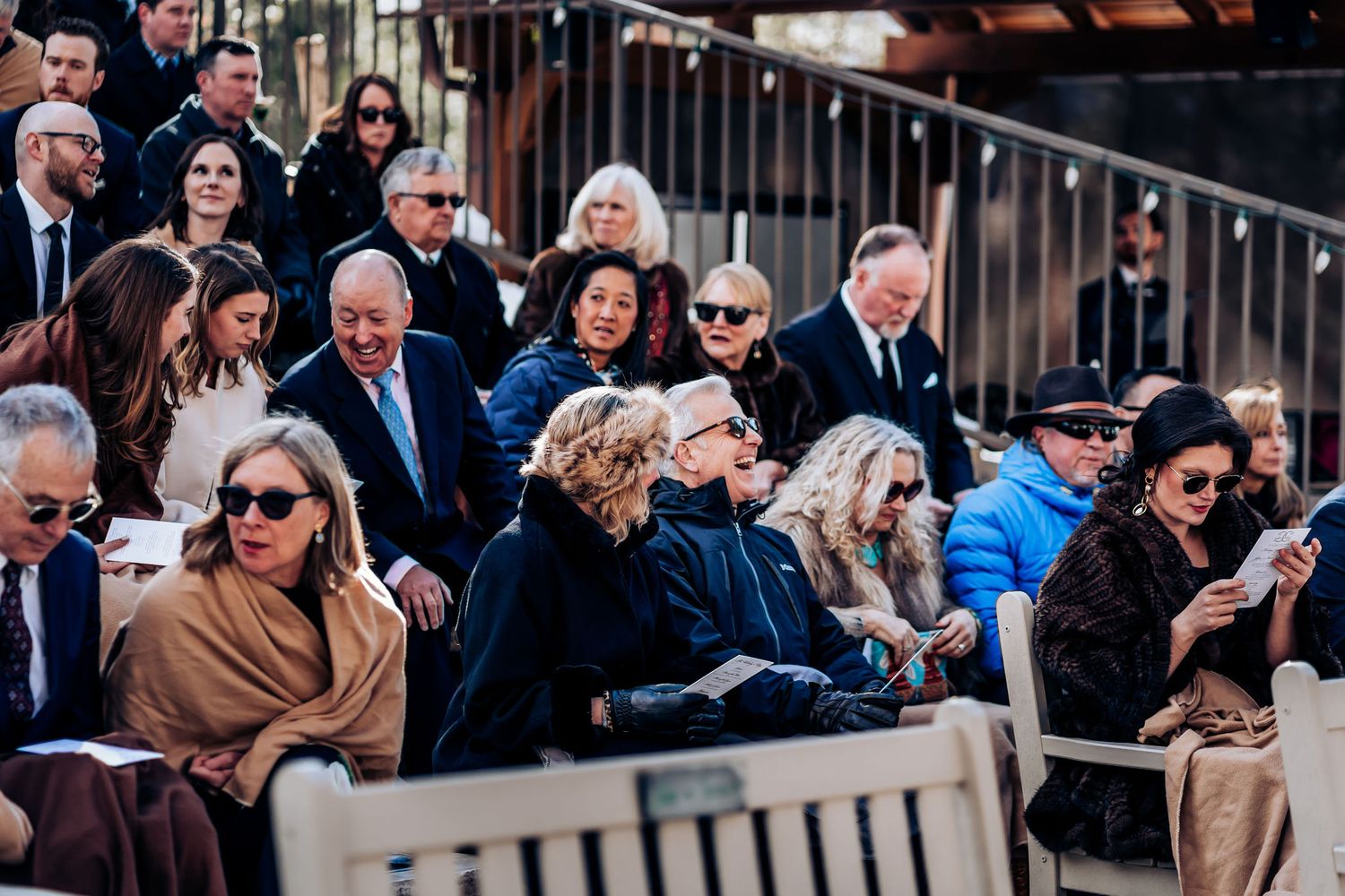 Wedding attendees seated in formal attire at an outdoor ceremony venue.