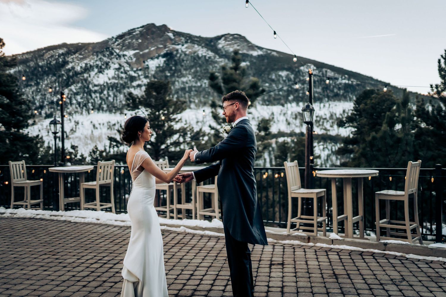 Couple dancing on a mountain terrace with snow-covered peaks and high-top tables in view.