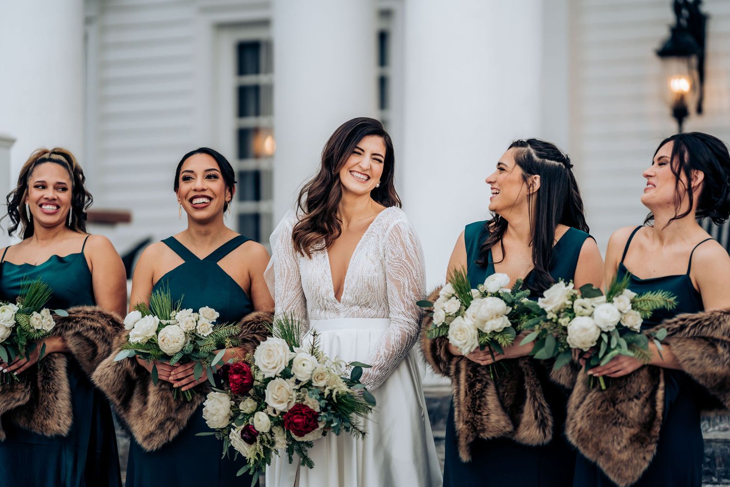 Bridesmaids in emerald dresses holding burgundy bouquets share a joyful moment.