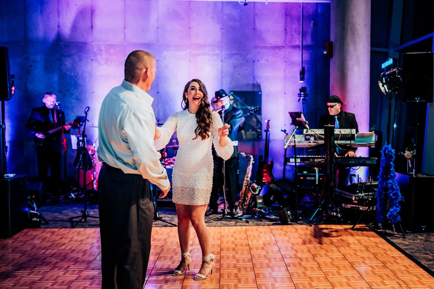 Couples dance on a wooden floor with a live band performing in the background.